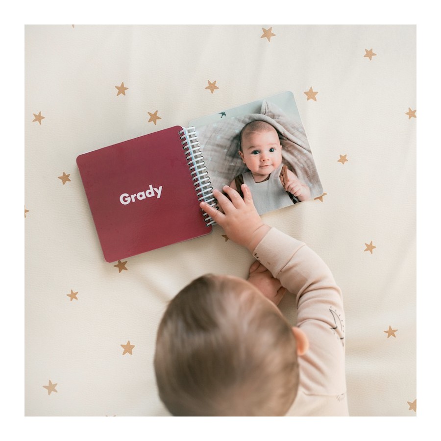 Baby turning the pages of a personalized photo board book with a white spiral binding